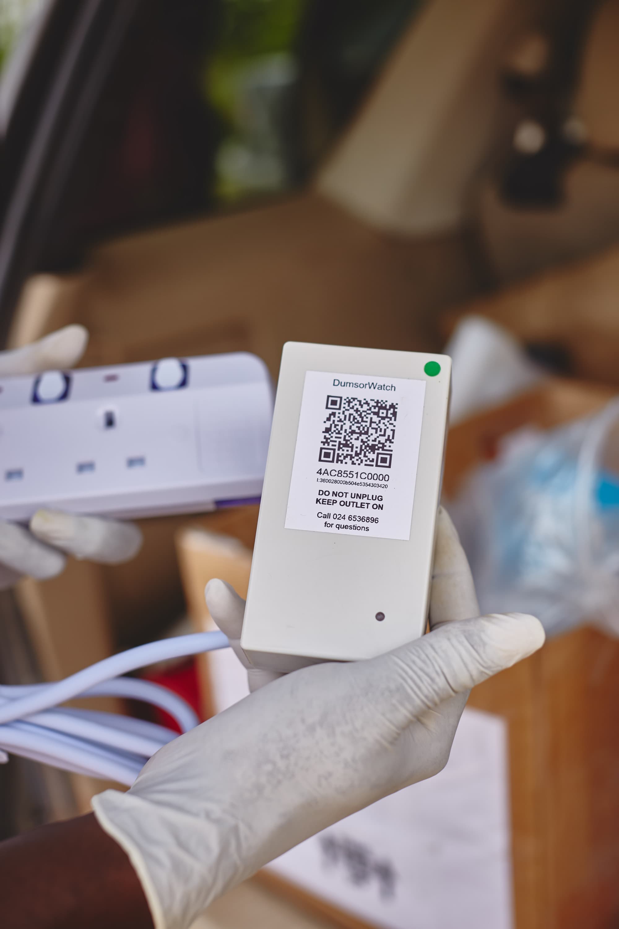 A PowerWatch sensor as shown during a project in Accra. It's a white box with a plug and a QR code sticker on the back.